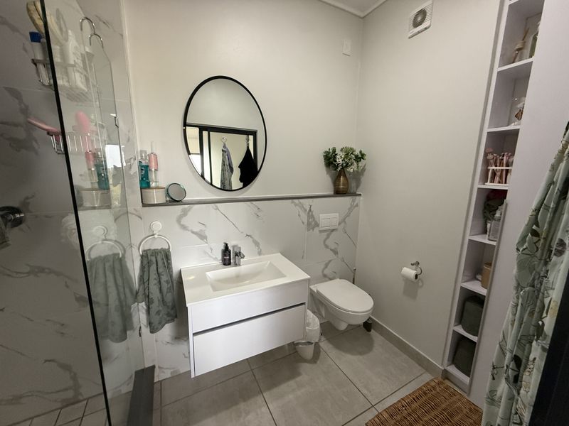 Modern bathroom featuring a wall-mounted vanity, wall-hung toilet with concealed cistern, glass shower enclosure, and built-in shelving with marble-look wall tiling.