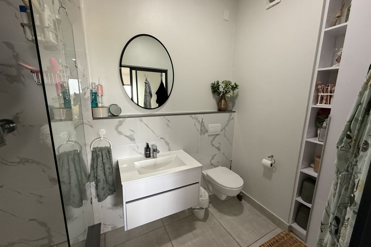 Modern bathroom featuring a wall-mounted vanity, wall-hung toilet with concealed cistern, glass shower enclosure, and built-in shelving with marble-look wall tiling.