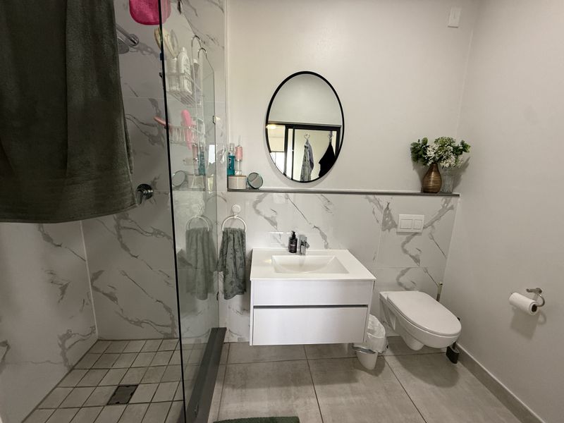 Modern bathroom featuring a wall-mounted vanity, wall-hung toilet, and a spacious walk-in shower with marble-look tiling and a glass enclosure.