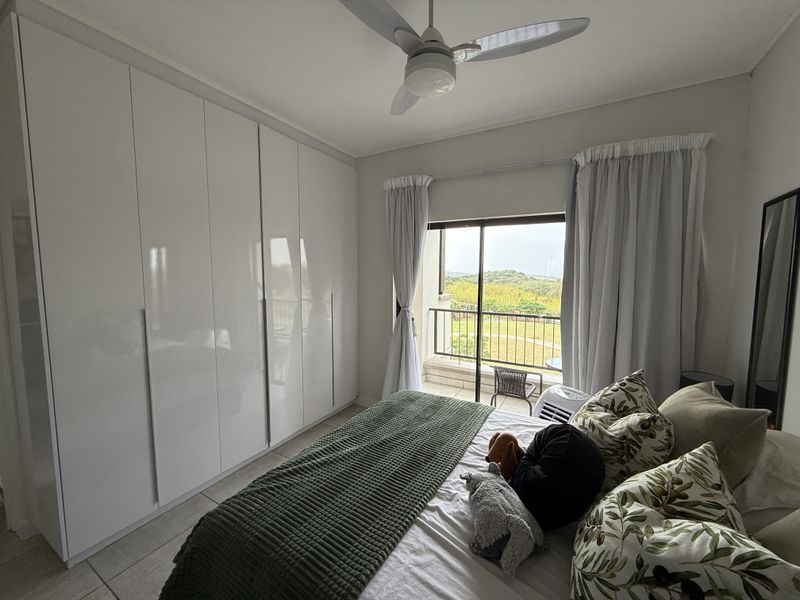 A well-maintained bedroom featuring floor-to-ceiling built-in cupboards, a ceiling fan, and direct access to a private balcony with scenic views.