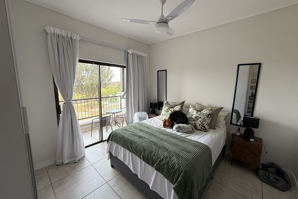 A well-lit bedroom featuring tiled flooring, a ceiling fan, and a sliding glass door providing access to an outdoor balcony area.