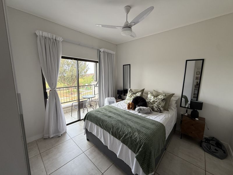 A well-lit bedroom featuring tiled flooring, a ceiling fan, and a sliding glass door providing access to an outdoor balcony area.