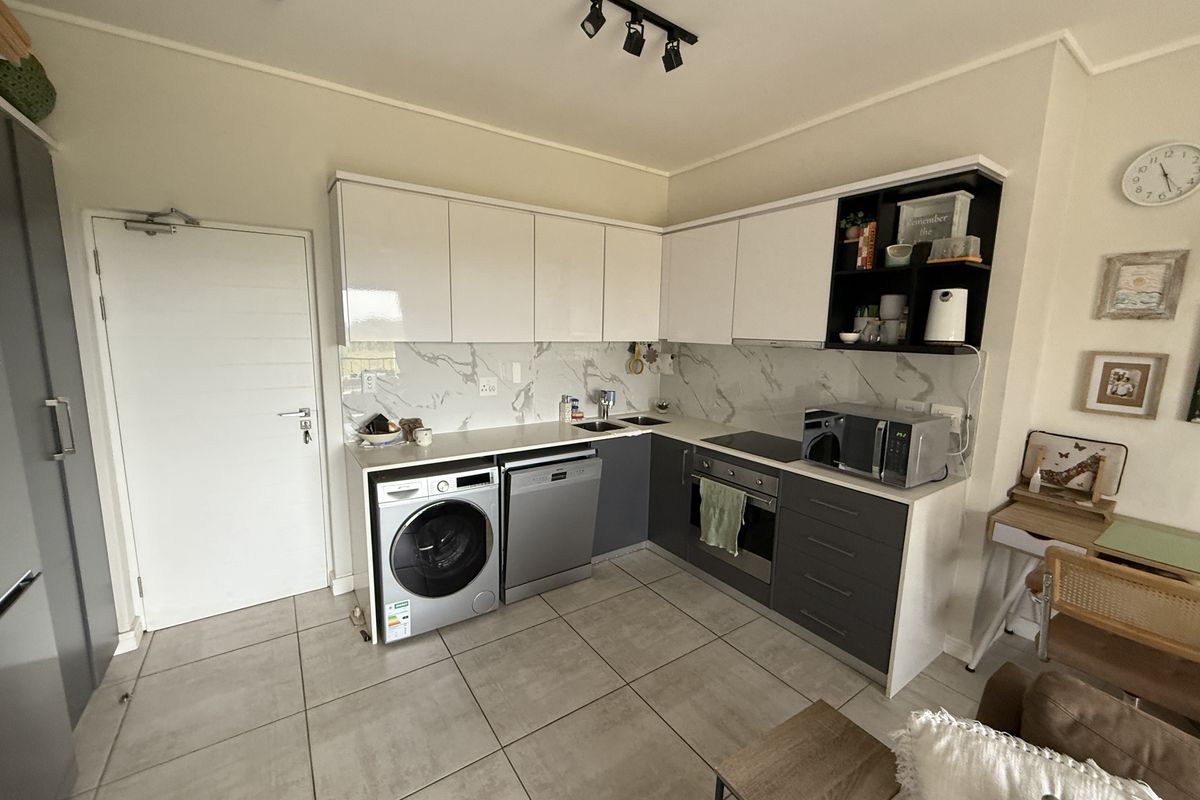 Modern kitchen featuring sleek white and grey cabinetry, marble-look splashback, integrated appliances, and tiled flooring in an open-plan layout.