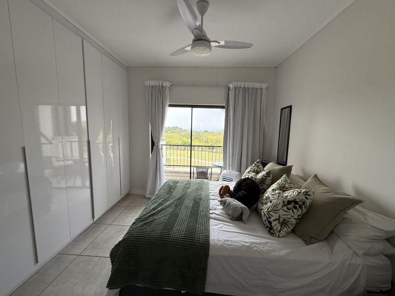 A well-maintained bedroom featuring floor-to-ceiling built-in cupboards, a ceiling fan, and a sliding glass door providing access to a balcony with scenic views.