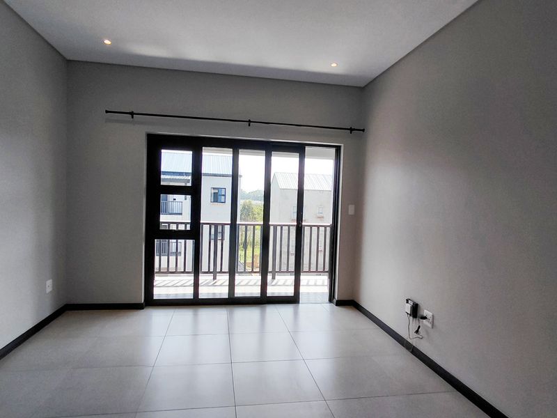 A bright, empty living room featuring modern tiled flooring, recessed lighting, and a large sliding glass door providing access to a balcony.