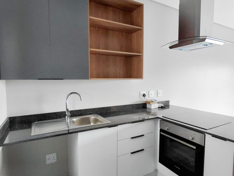 Modern kitchen featuring sleek two-tone cabinetry, granite countertops, stainless steel sink, and integrated appliances including an oven, hob, and extractor fan.