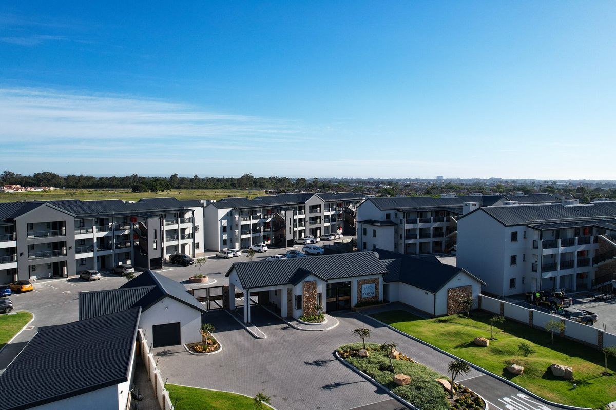 Aerial view of a modern apartment complex featuring multiple residential blocks, a secure gated entrance, paved driveways, and well-maintained landscaped grounds.
