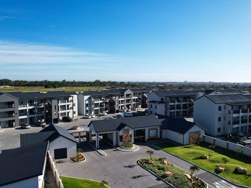 Aerial view of a modern apartment complex featuring multiple residential blocks, a secure gated entrance, paved driveways, and well-maintained landscaped grounds.