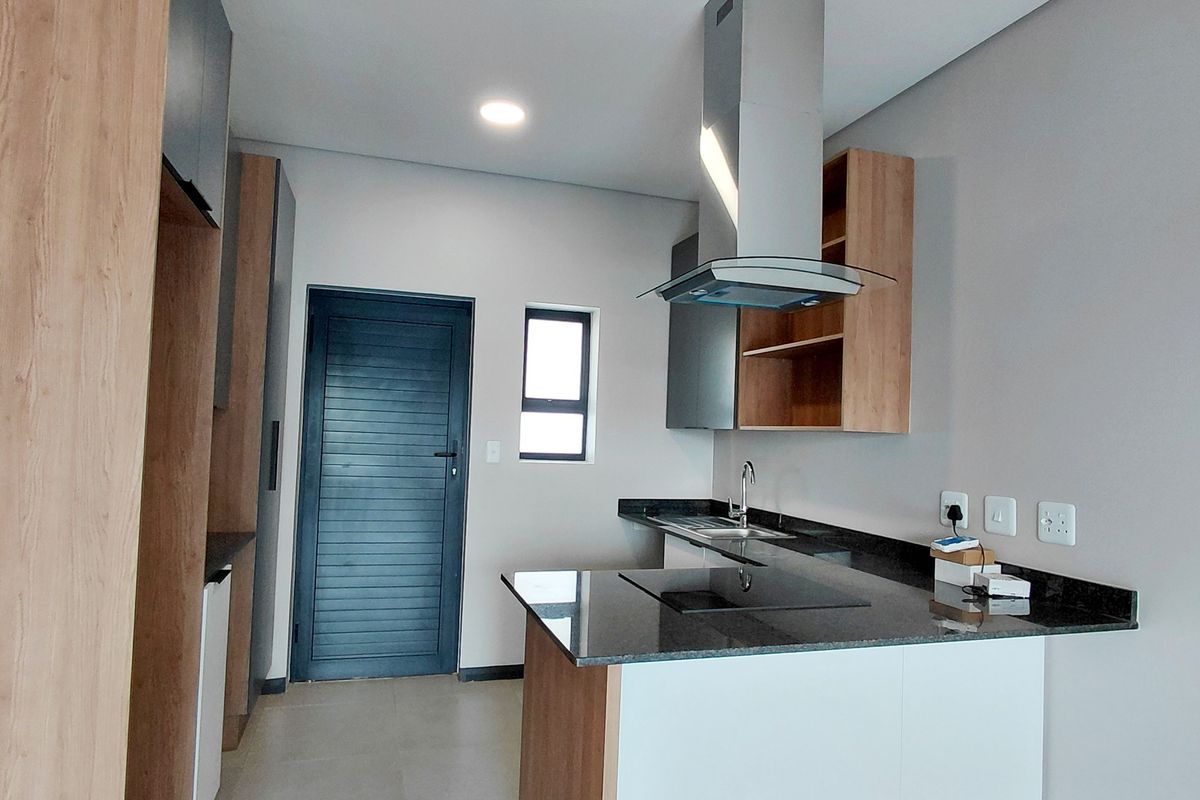 Modern kitchen featuring sleek wood-tone and white cabinetry, granite countertops, integrated hob, and stainless steel extractor fan in a clean, contemporary space.