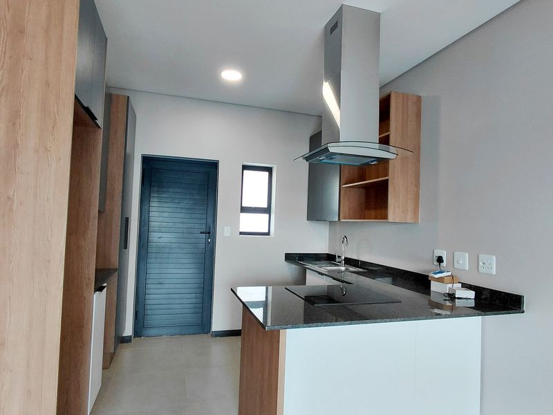 Modern kitchen featuring sleek wood-tone and white cabinetry, granite countertops, integrated hob, and stainless steel extractor fan in a clean, contemporary space.