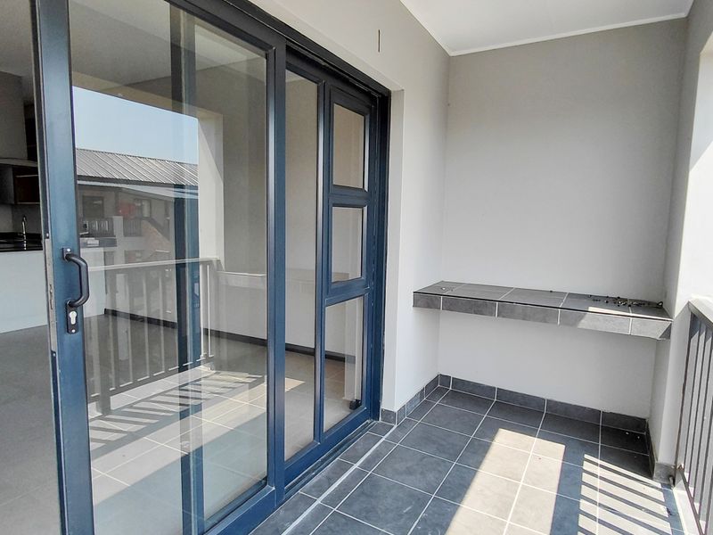 A clean, modern balcony featuring tiled flooring, a built-in tiled shelf, and large sliding glass doors providing access to the interior living space.