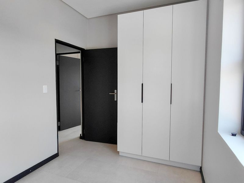 A clean, modern bedroom featuring neutral tiled flooring, recessed lighting, and a sleek white built-in wardrobe with contrasting black door frames.