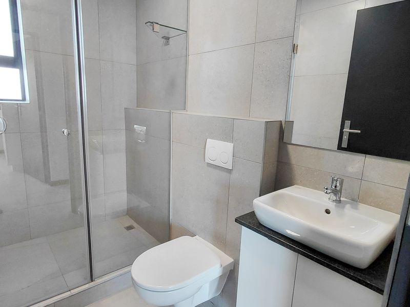 Modern bathroom featuring a wall-mounted toilet, glass-enclosed shower, and a sleek vanity with a vessel sink and wall-mounted mirror.