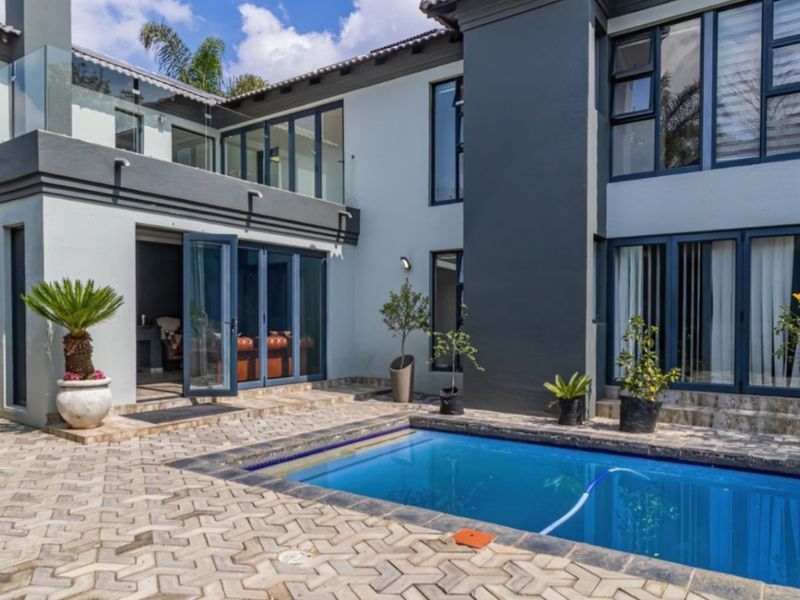 A modern double-storey home exterior featuring a paved pool area, glass balustrades, and large aluminium bi-fold doors leading to the interior living space.