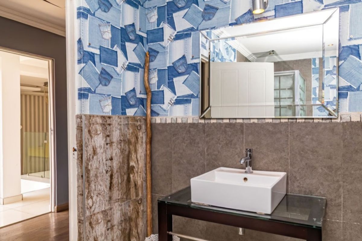 A bathroom featuring a modern vessel sink, chrome faucet, and a large wall-mounted mirror, accented by unique denim-patterned wallpaper and neutral wall tiles.