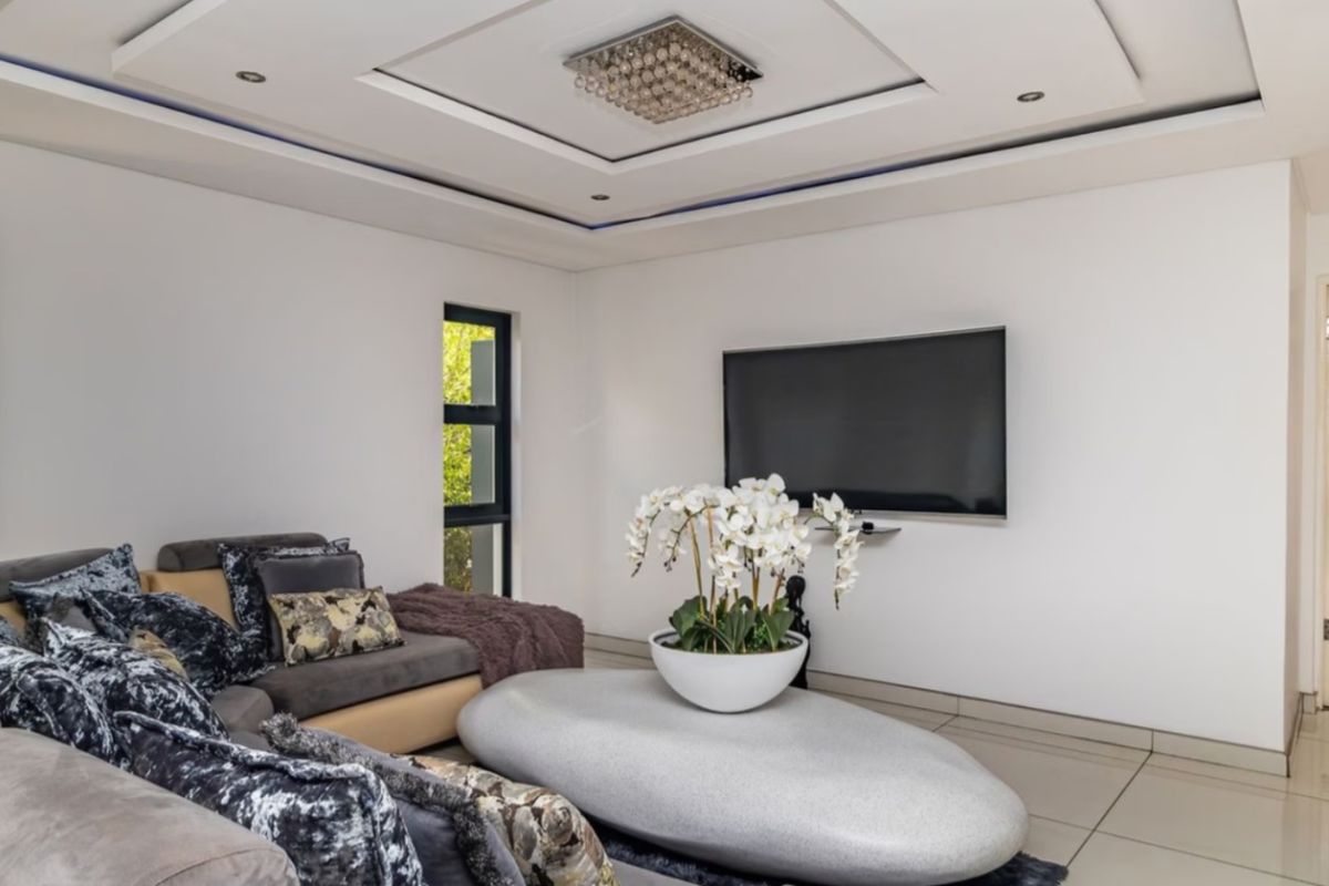A modern living room featuring a recessed ceiling with integrated lighting, large aluminium windows, and polished floor tiles.