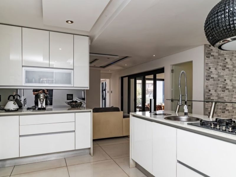 Modern kitchen featuring high-gloss cabinetry, stone countertops, a central island with a gas hob, and integrated appliances, seamlessly flowing into the living area.