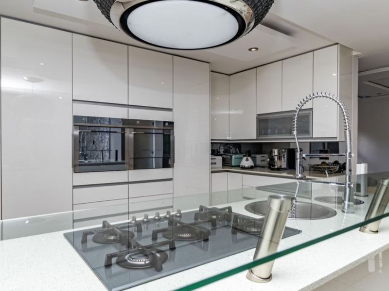 Modern kitchen featuring high-gloss cabinetry, a central island with a gas hob, quartz countertops, and integrated built-in ovens.