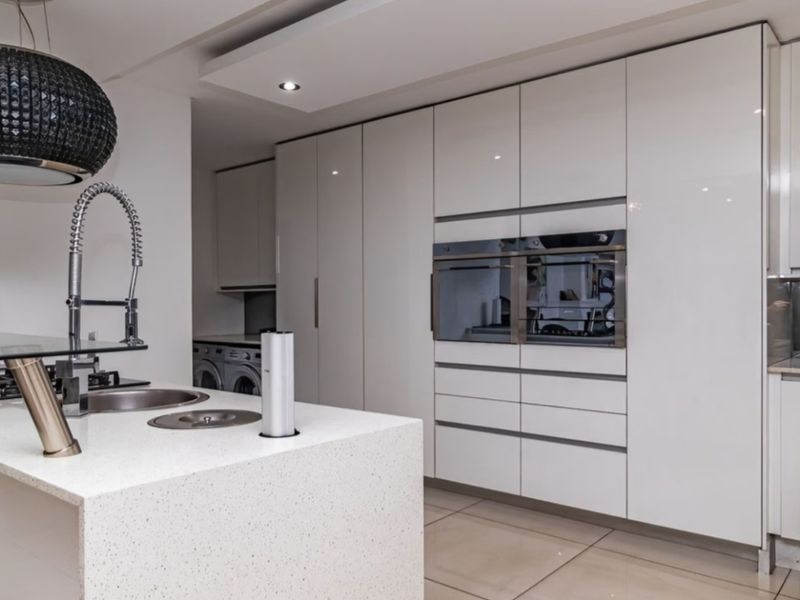 Modern kitchen featuring high-gloss cabinetry, stone countertops, a central island with integrated sink, and built-in appliances including an oven and microwave.