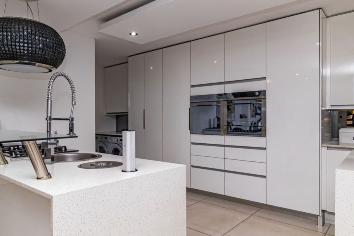 Modern kitchen featuring high-gloss cabinetry, stone countertops, a central island with integrated sink, and built-in appliances including an oven and microwave.