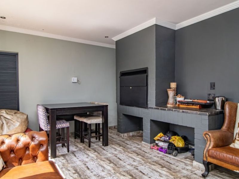 Covered patio area featuring a built-in braai, tiled flooring, and recessed lighting, offering a functional space for outdoor entertaining.