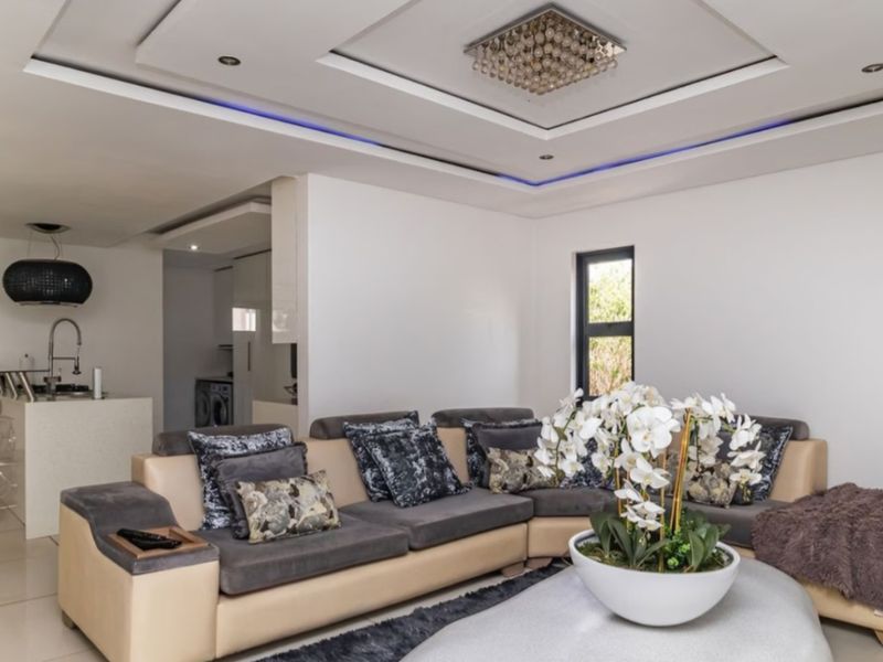 Modern open-plan living area featuring a contemporary kitchen island, recessed ceiling with ambient LED lighting, and large aluminium-framed windows overlooking the garden.