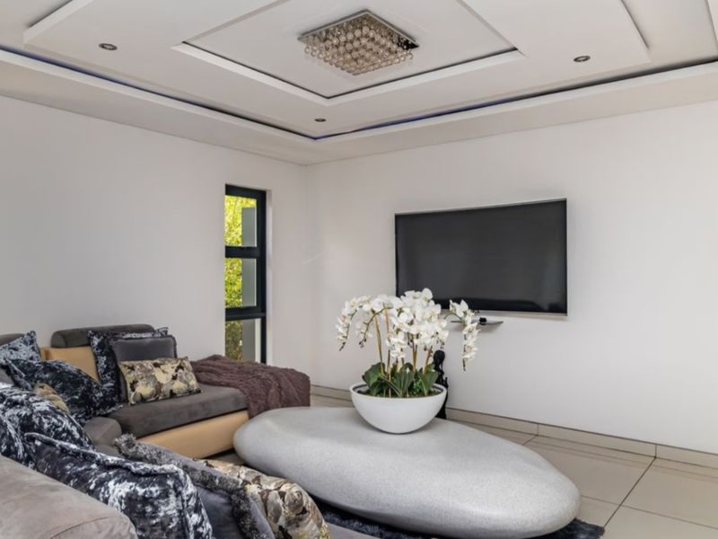 A modern living room featuring a recessed ceiling with integrated lighting, large aluminium windows, and polished floor tiles.
