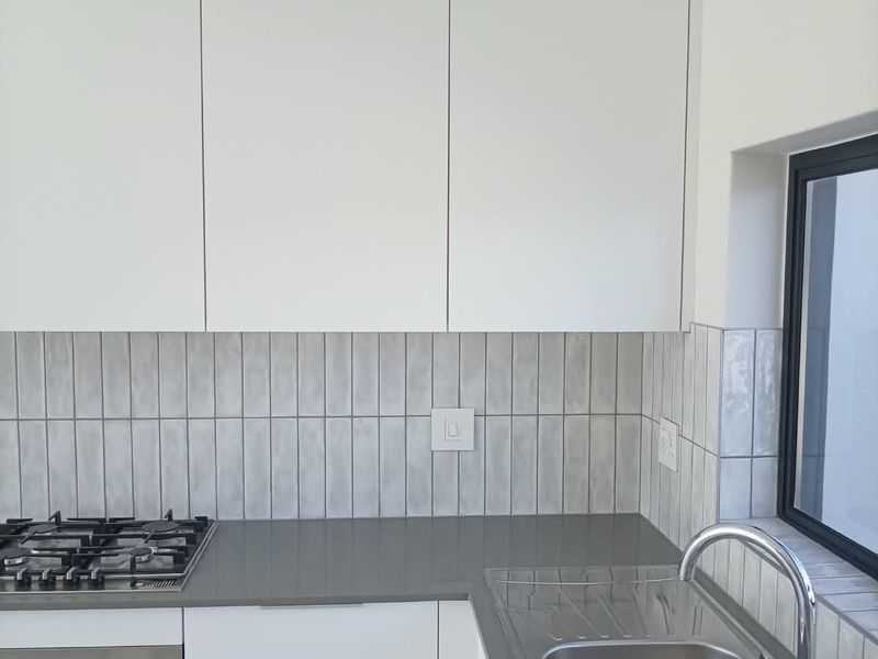 Modern kitchen featuring white cabinetry, stone countertops, a gas hob, built-in oven, and a stainless steel double sink with a tiled backsplash.