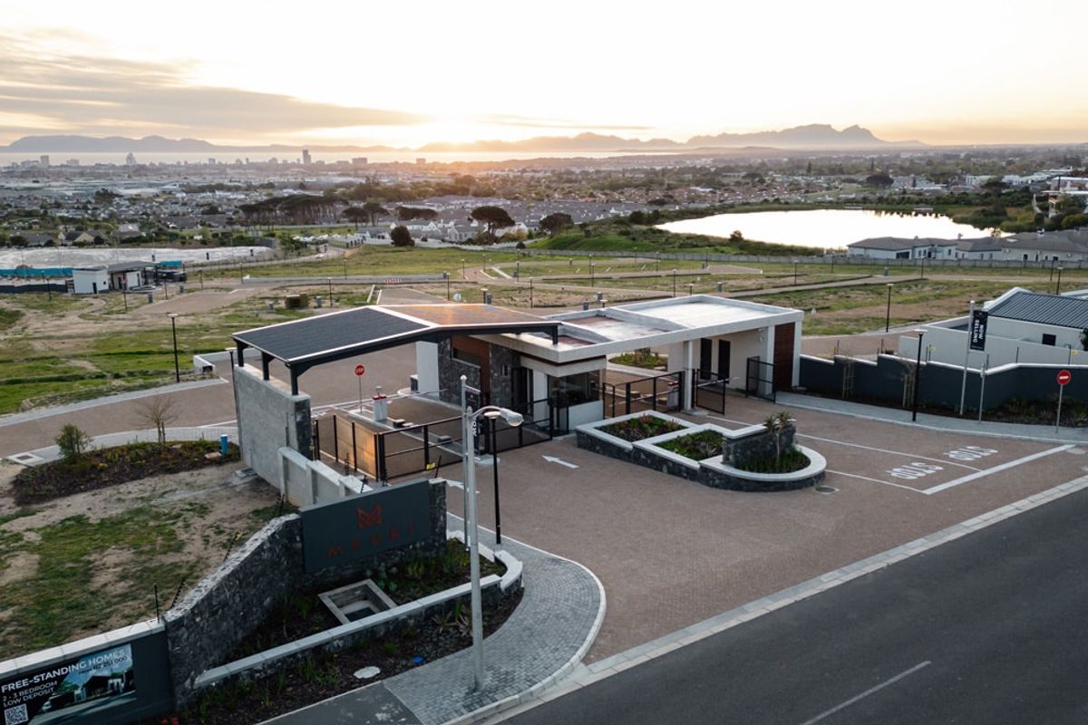Aerial view of a modern residential estate security entrance featuring stone cladding, solar-powered roofing, and paved access roads.