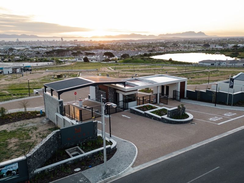Aerial view of a modern residential estate security entrance featuring stone cladding, solar-powered roofing, and paved access roads.