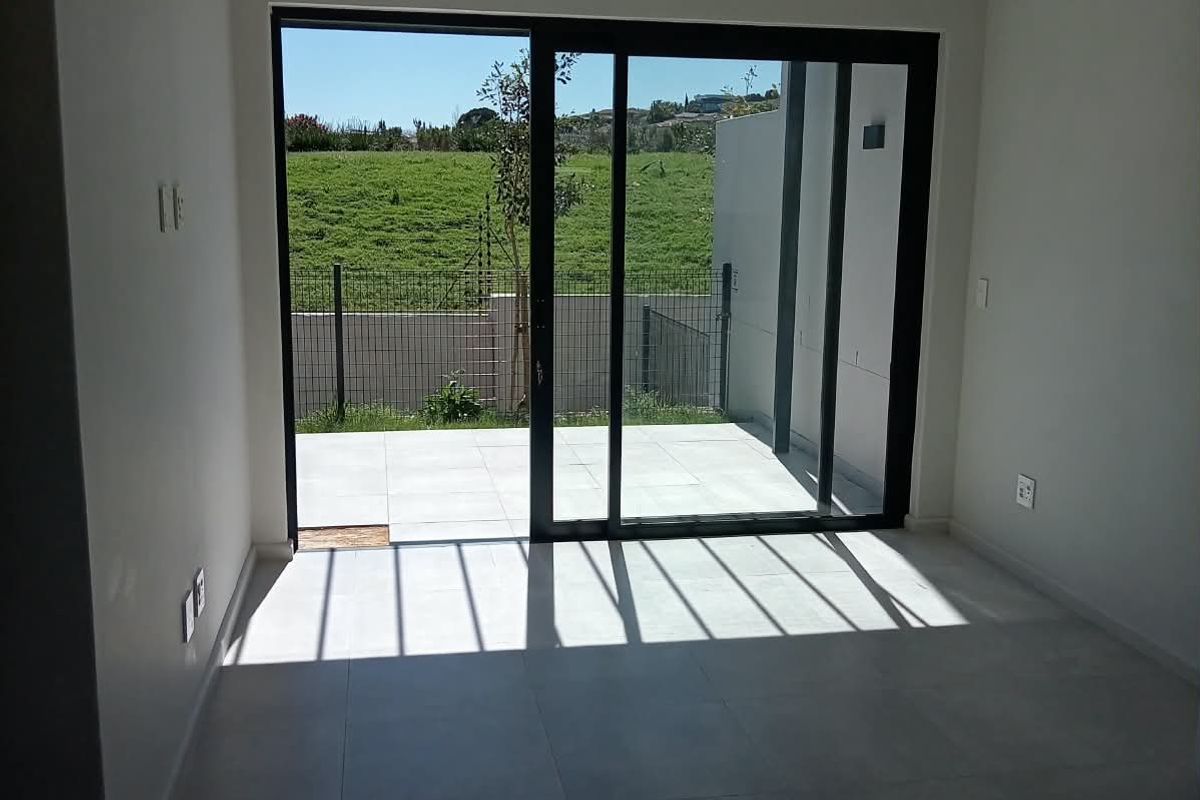 A bright, empty living room featuring large sliding glass doors that open onto a paved patio area with a view of the garden.