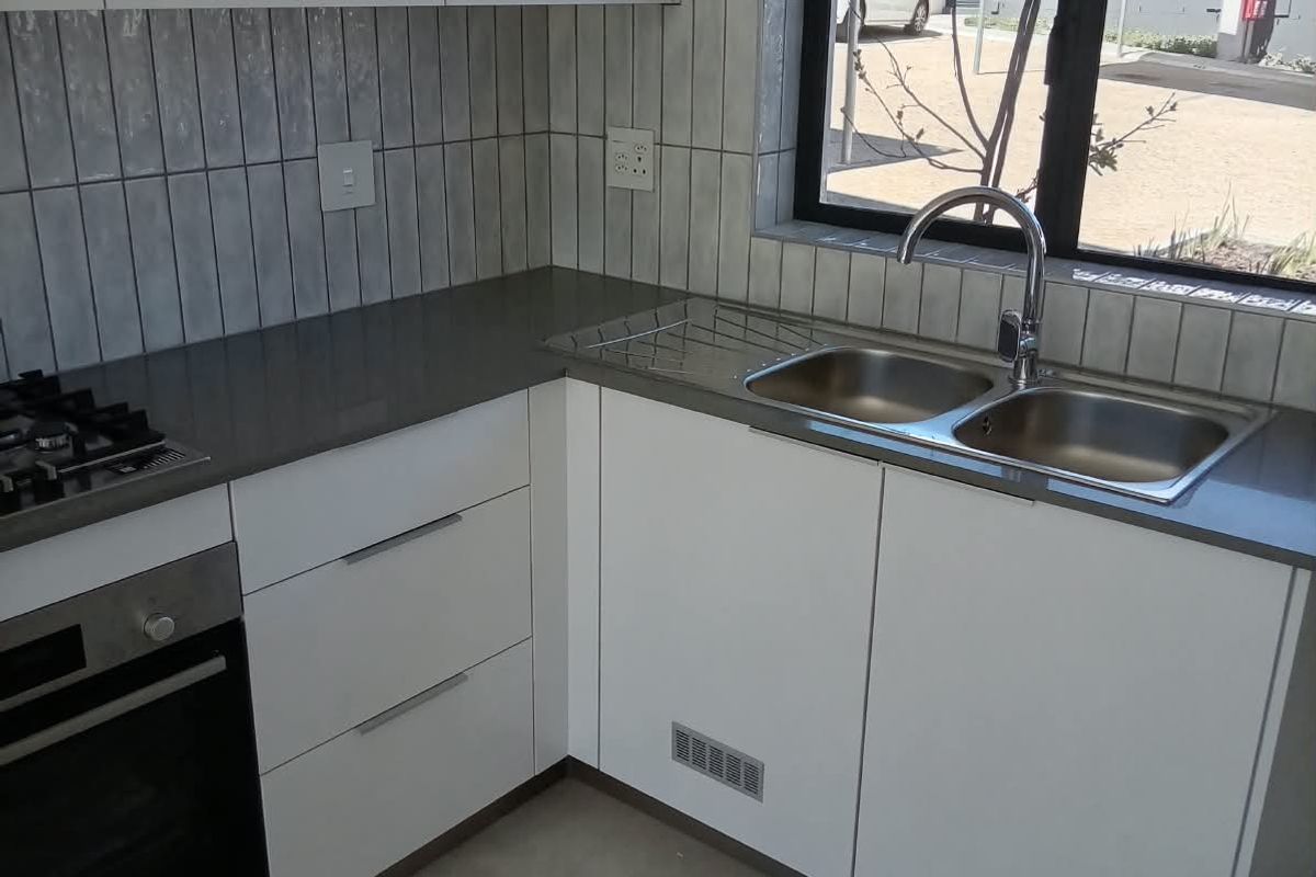 Modern kitchen featuring white cabinetry, stone countertops, a built-in oven, gas hob, and a double sink with a view of the exterior.
