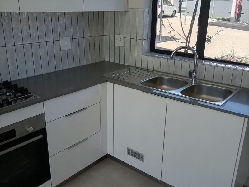 Modern kitchen featuring white cabinetry, stone countertops, a built-in oven, gas hob, and a double sink with a view of the exterior.