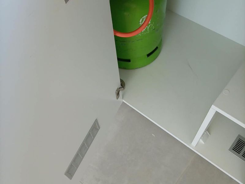 Interior view of a kitchen cabinet storage area featuring a gas cylinder with an emergency shut-off valve label and integrated ventilation.