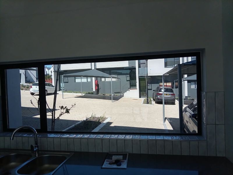 A view from the kitchen sink looking out onto the apartment complex parking area and exterior facade.