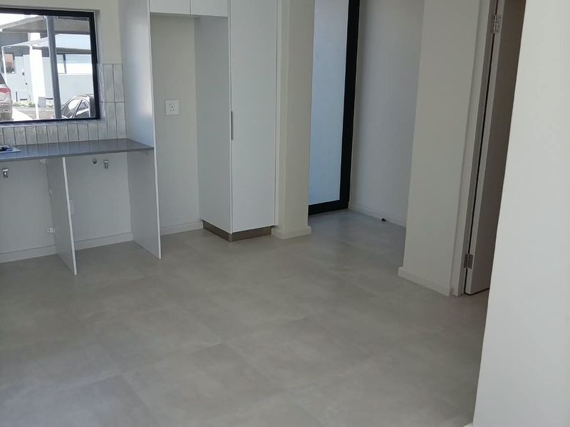A clean, modern, and empty kitchen area featuring neutral tiled flooring, built-in white cabinetry, and a functional countertop with a tiled backsplash.