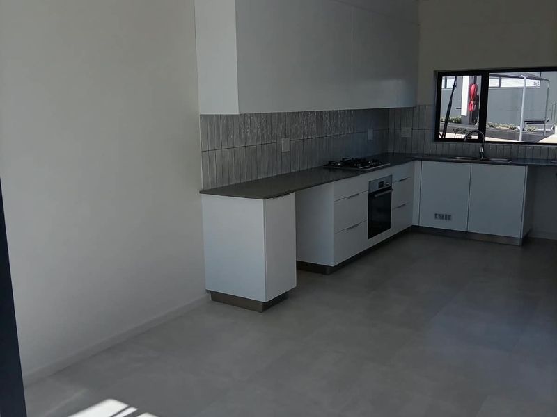 Modern, empty kitchen featuring sleek white cabinetry, built-in oven, gas hob, and neutral tiled flooring, offering a clean and functional space.