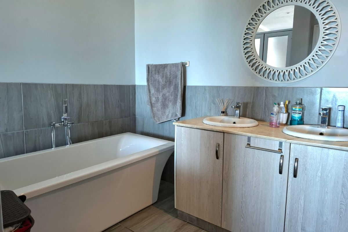 Modern bathroom featuring a freestanding bathtub, double vanity with built-in cabinetry, and neutral tiled finishes.