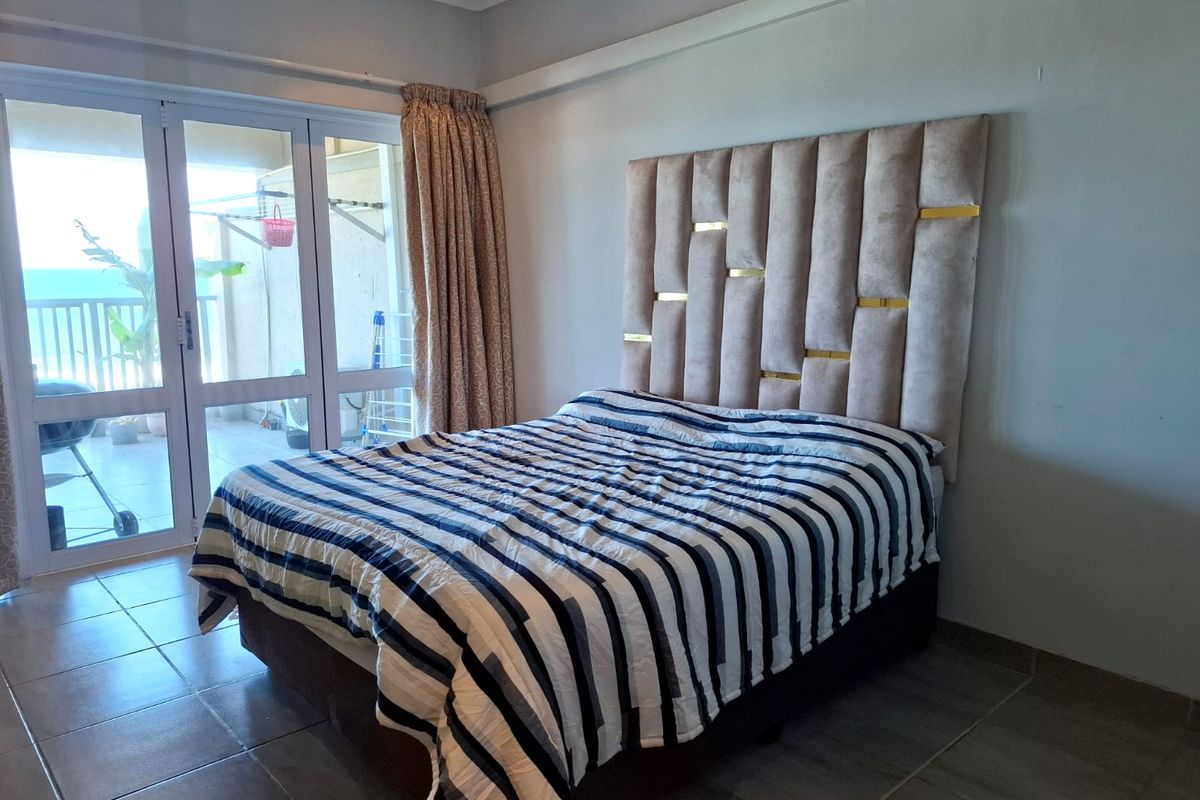 A well-maintained bedroom featuring tiled flooring, a wall-mounted air conditioning unit, and direct access to a private balcony through sliding glass doors.