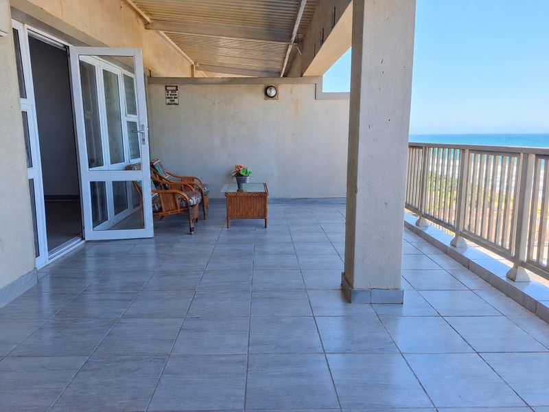 Spacious covered balcony featuring tiled flooring, a metal balustrade, and direct ocean views, providing an ideal outdoor relaxation area.