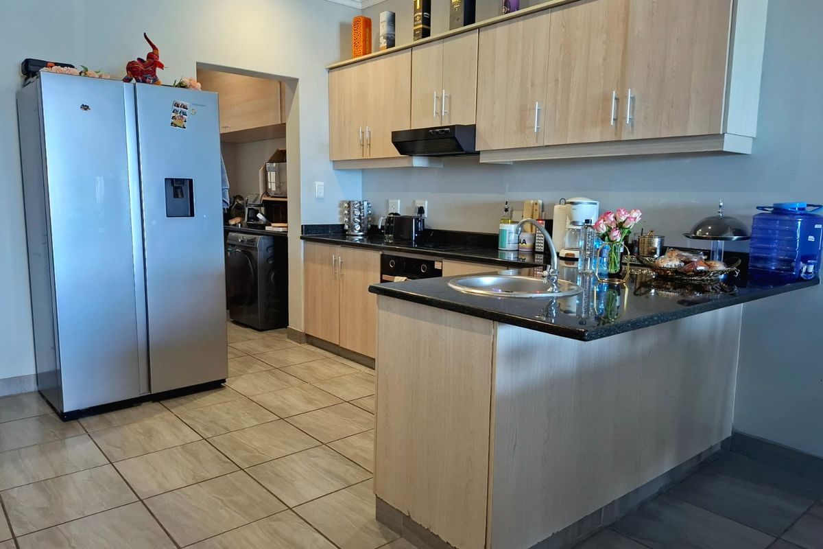 Functional kitchen featuring light wood-finish cabinetry, dark granite countertops, integrated oven, extractor fan, and tiled flooring, with an adjacent scullery area.