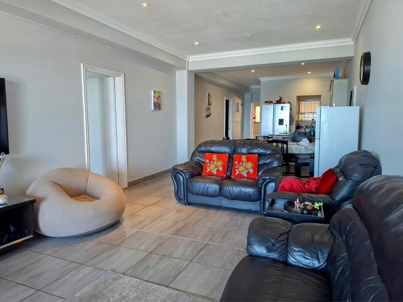 Spacious open-plan living area featuring tiled flooring, recessed downlighting, and decorative cornicing, seamlessly connecting the lounge to the kitchen space.