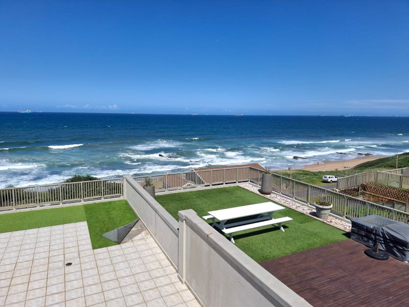 Spacious elevated balcony featuring a combination of tiled flooring, timber decking, and artificial grass, offering expansive ocean views and secure perimeter railing.
