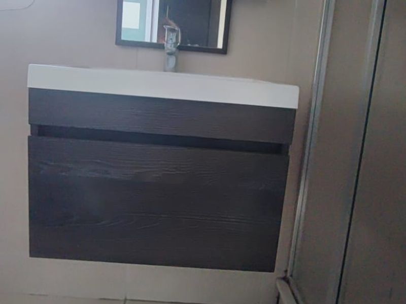 A modern bathroom featuring a wall-mounted vanity with a basin, a mirror, and a glass shower enclosure with tiled flooring.