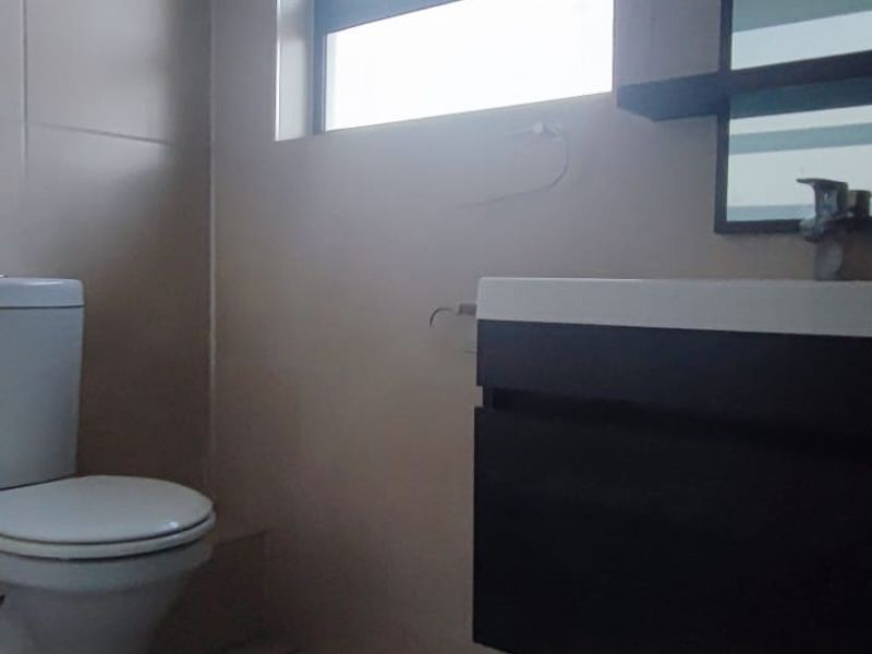 A functional bathroom featuring a wall-mounted vanity with basin, tiled flooring, and a toilet, illuminated by natural light from a window.