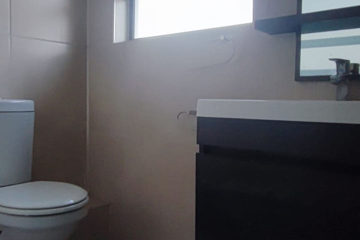 A functional bathroom featuring a wall-mounted vanity with basin, tiled flooring, and a toilet, illuminated by natural light from a window.