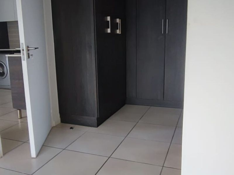 A clean, empty hallway featuring dark wood-finish built-in cupboards and neutral floor tiles, providing ample storage space.