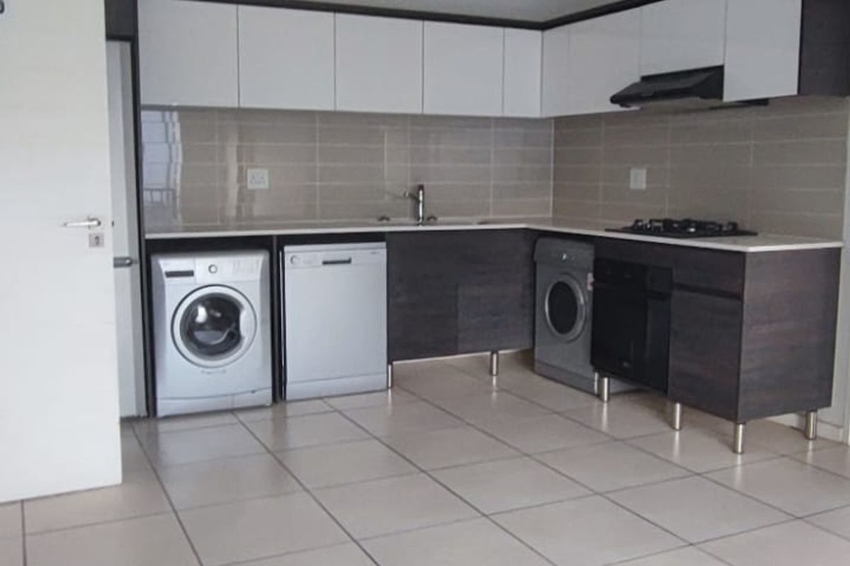 Modern kitchen featuring sleek two-tone cabinetry, tiled backsplash, built-in oven, gas hob, and integrated appliance spaces with neutral floor tiles.