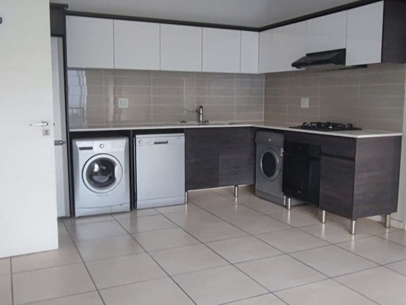 Modern kitchen featuring sleek two-tone cabinetry, tiled backsplash, built-in oven, gas hob, and integrated appliance spaces with neutral floor tiles.