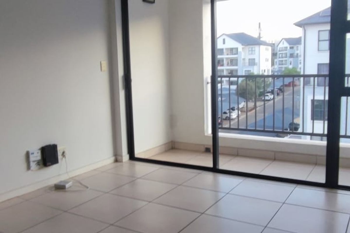 An empty living room featuring neutral tiled flooring and a large sliding glass door providing access to a private balcony.